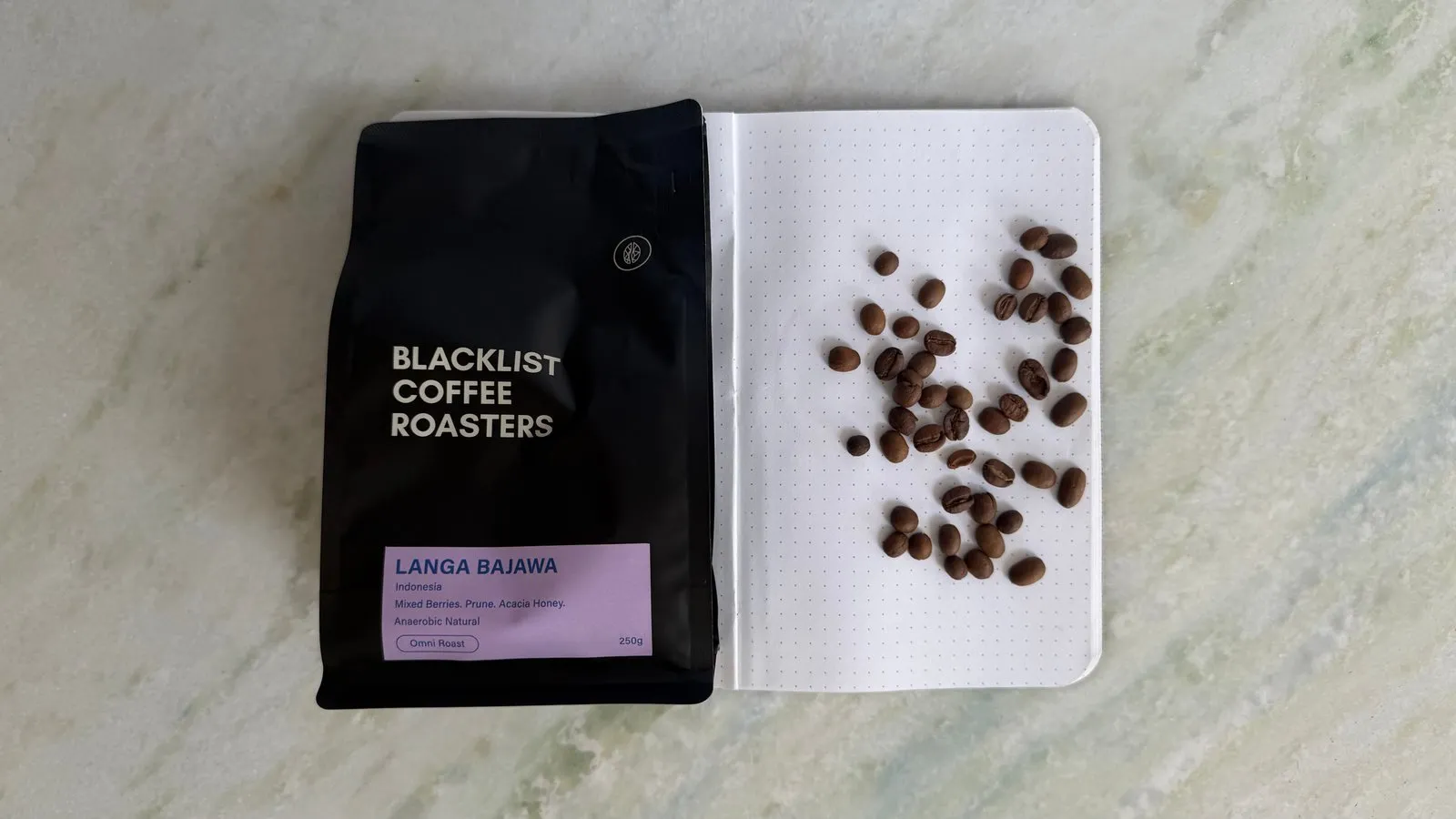Black coffee bag and coffee beans on a white dotted notebook.