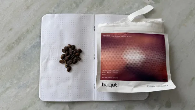 Close-up of coffee beans on an open notebook with a coffee package on a light grey surface.