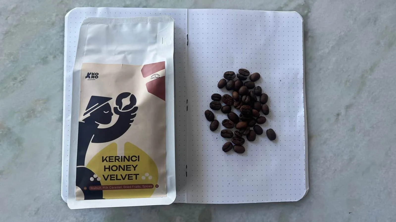 A close-up of dark roasted coffee beans next to a packet of Kerinci Honey Velvet tea, highlighting premium quality coffee and tea products for enthusiasts and connoisseurs.